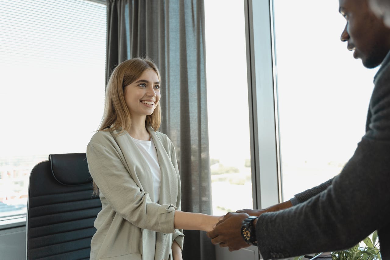 get-in-touch Woman smiling and shaking hands at a business office, signaling a successful job interview.